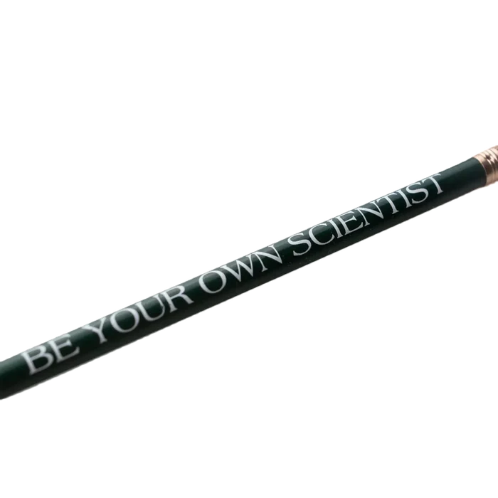 A green pencil with "BE YOUR OWN SCIENTIST" in white text, placed on top of the college-ruled Stay Curious Journal from the Stemcell Science Shop set.