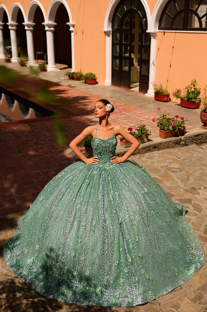 A woman in a mint green sparkly ball gown poses confidently in a courtyard with arched windows and potted flowers.