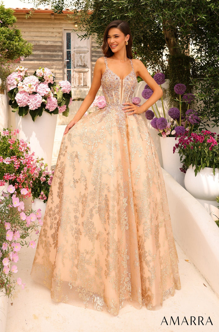 A model wears a gold ball gown with sparkling details, standing in a garden with pink and purple flowers.