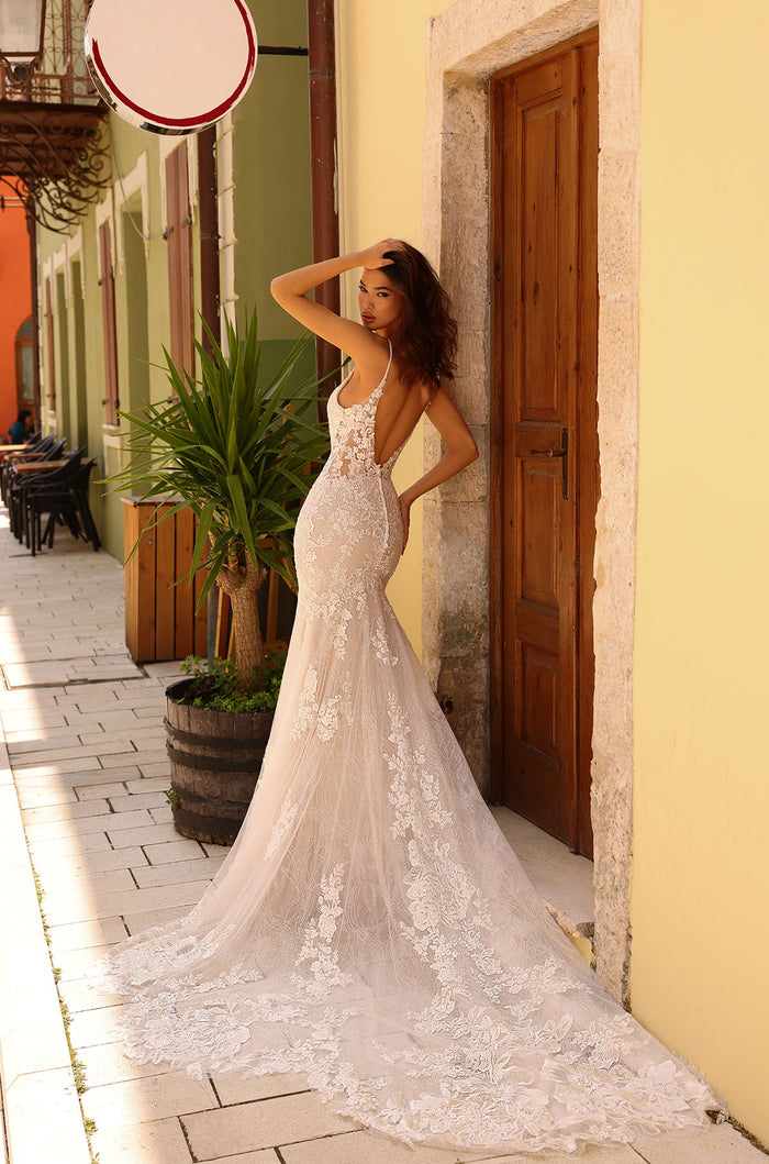 A bride in a lace mermaid wedding gown poses elegantly against a yellow wall with a wooden door.