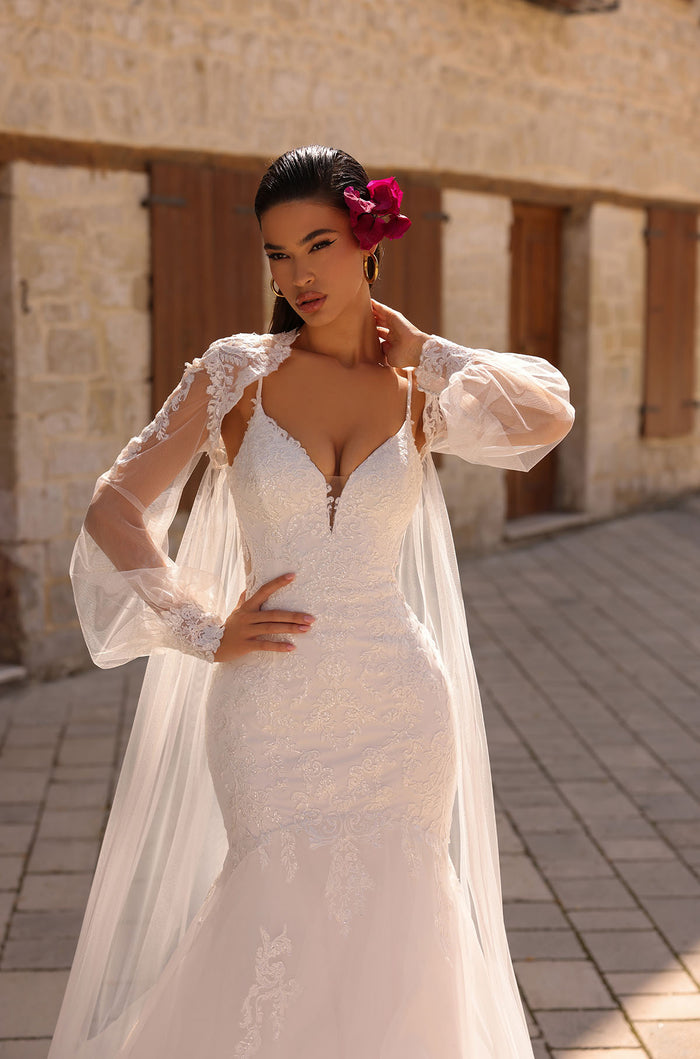 A bride in a white lace mermaid wedding dress with puff sleeves and a magenta flower in her hair.