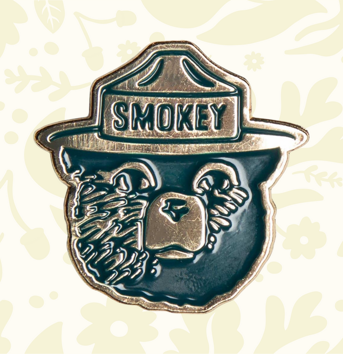 Smokey Bear enamel pin by Landmark Project shows Smokey’s face and ranger hat—perfect collectible for Smokey Bear fans.