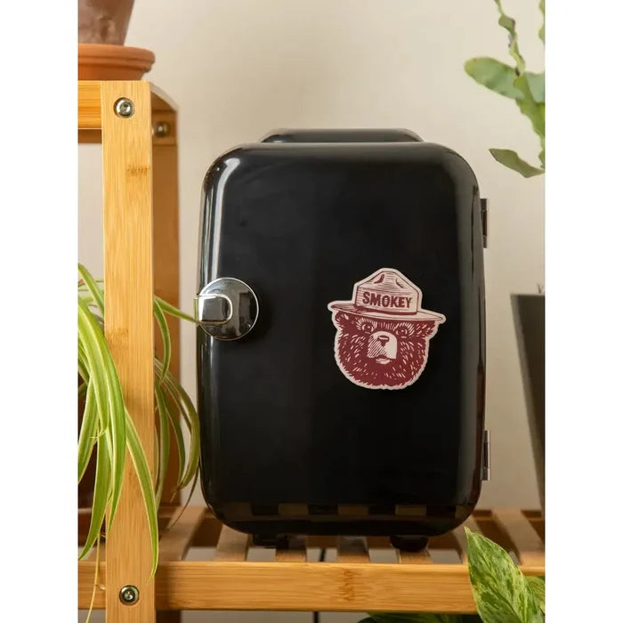 Illustration of a bear wearing a ranger hat labeled "Smokey," commonly known as Smokey Bear, associated with fire prevention—The Landmark Project Smokey Bear Face Magnet is perfect for showcasing your love for nature and conservation.