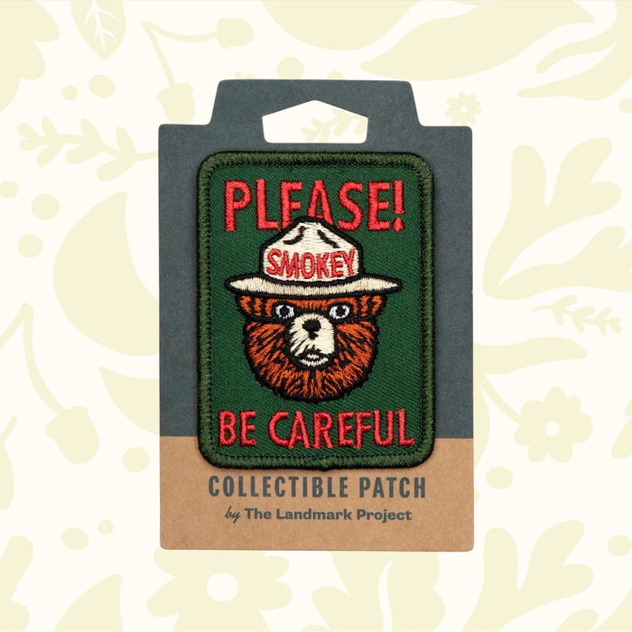 The official licensed "The Landmark Project Smokey Bear Patch - Please Becareful" from the USDA Forest Service features a collectible design of Smokey Bear with the text "PLEASE! BE CAREFUL." above and below him, supporting wildfire prevention education.