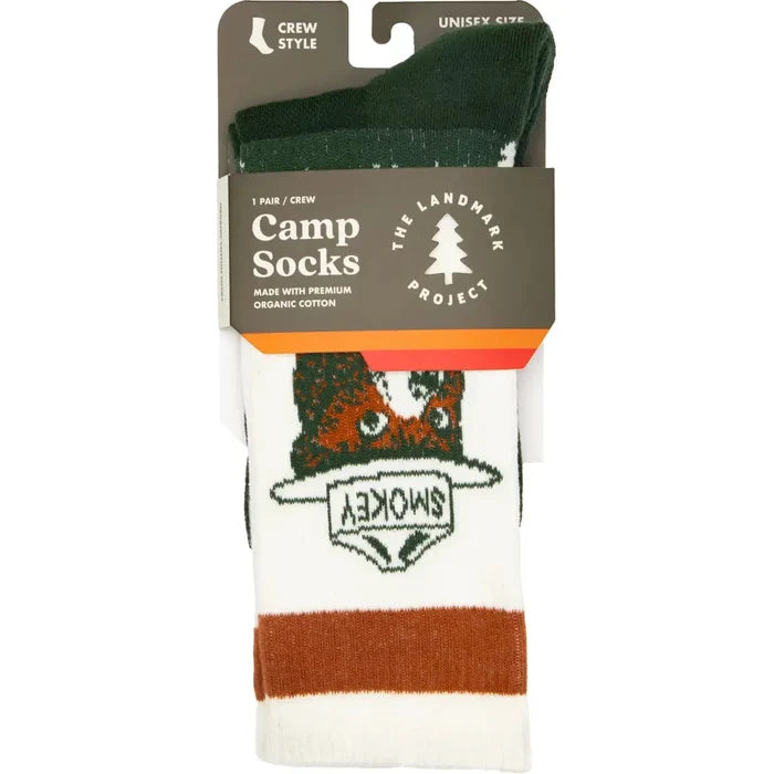 Close-up of The Landmark Project Smokey Bear Socks, crafted from green and white organic cotton, showcasing Smokey Bear in a ranger hat. The soles of the socks feature the phrase "Prevent Wildfires" alongside Smokey's logo.
