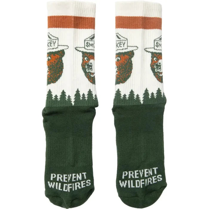 Close-up of The Landmark Project Smokey Bear Socks, crafted from green and white organic cotton, showcasing Smokey Bear in a ranger hat. The soles of the socks feature the phrase "Prevent Wildfires" alongside Smokey's logo.