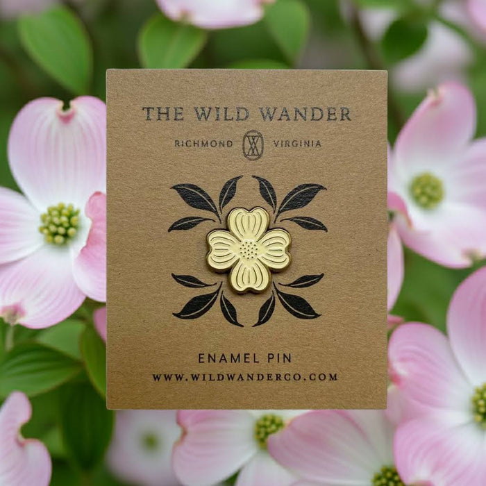 Forager Provisions LTD ivory and antique gold dogwood flower enamel pin on a kraft backing card against pink flowers.