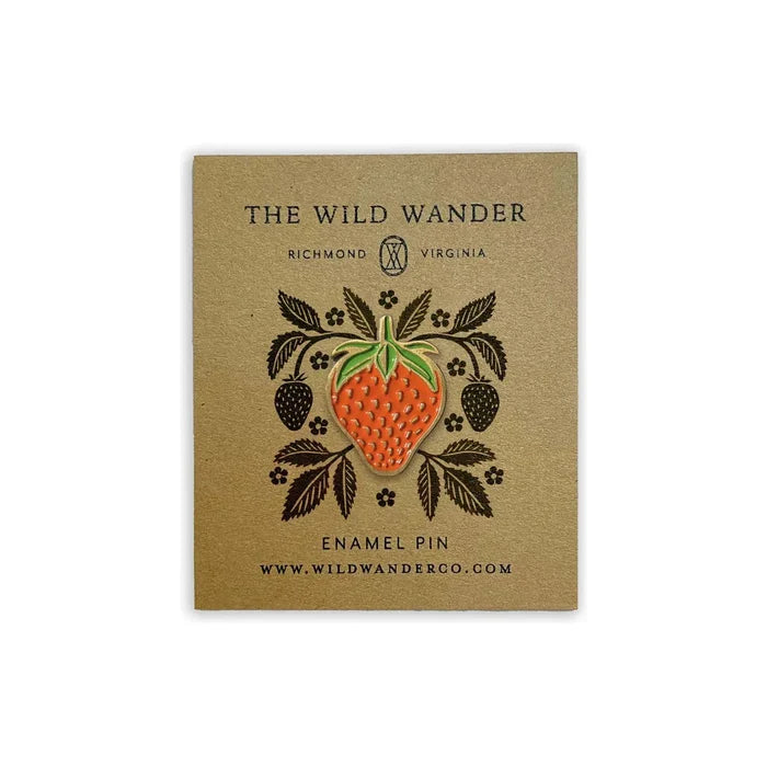 The Wild Wander Strawberry Lapel Pin features a custom illustrated enamel design in the shape of a strawberry with leaves. Branded under "The Wild Wander," it includes location and website information. The pin is packaged plastic-free and comes with a secure rubber backer for durability.