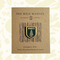 Green enamel pin with fir tree, WANDER text, on The Wild Wanders branded card—forest nature hiking accessory.