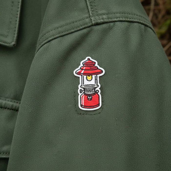 Forager Provisions LTD embroidered camping lantern patch in red and yellow, iron-on design on a green canvas jacket.