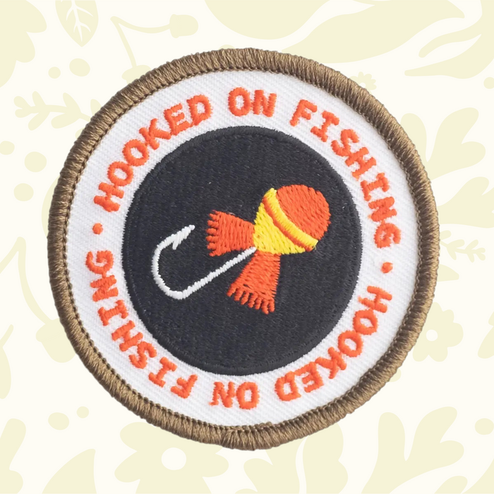 Forager Provisions LTD Hooked On Fishing embroidered patch with a round design, orange text, and a fishing hook icon.