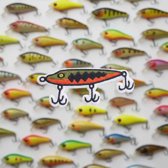 Forager Provisions LTD embroidered fishing lure patch with orange and green details on a background of lure patterns
