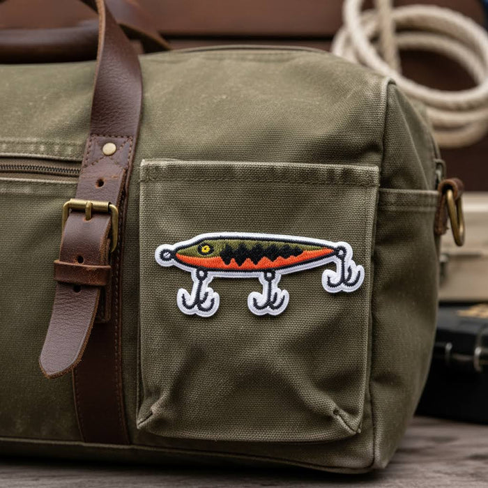Forager Provisions LTD embroidered fishing lure patch attached to an olive green canvas bag with leather straps