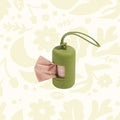 Wild One Moss Dog Poop Bag Dispenser with handle, on floral backdrop. Perfect holder for bags. Stylish pet accessory.