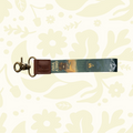 Wildtree Smokey Bear keychain—leather/fabric, clasp, camera charm, forest scene, floral pattern. Outdoor adventure gift.